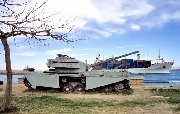 埃及苏伊士运河边的旧生锈的装甲坦克 船尾有路过的集装箱船 免版税图库照片