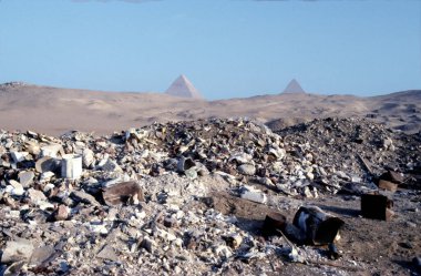 Mısır 'daki Giza piramit kompleksinde çevre kirliliği, arka planda büyük piramitler bulunan sarı kumda yatan yıpranmış eski plastik şişeler,