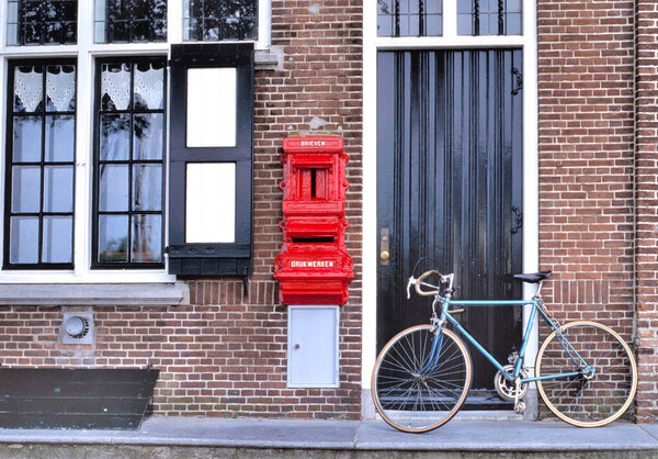 Старый красный почтовый ящик, установленный в кирпичной стене дома с текстом BRIEVEN (буквы) и DRUKWERKEN (пресс-работа или печатная продукция) с рядом с ним старомодный велосипед 