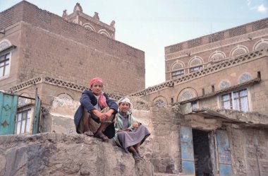 SANAA, YEmen-APRIL 25 Nisan 2011: Başkentin merkezindeki tipik Yemen evlerinin önündeki bir kayanın üzerinde oturan iki adam
