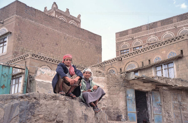 SANAA, YEMEN-APRIL 25,2011: Двое мужчин сидят на скале перед типичными йеменскими домами в центре столицы