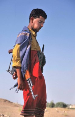 MARIB, YEMEN-APRIL 28, 2011: Açık mavi gökyüzüne karşı geleneksel giysili adam Kalaşnikov ve Jambiya ile