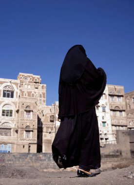 Peçeli Müslüman bir kadın Sana caddesinde yürüyor, Yemen. Arka planda tipik Yemen evleri. 