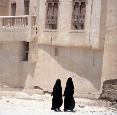 Peçeli Müslüman kadınlar Yemen 'in başkenti Sanaa' da bir sokakta yürüyorlar. Arka planda tipik Yemen evleri. 