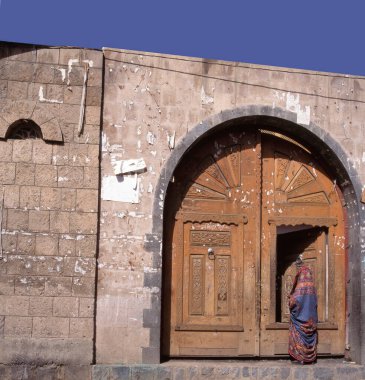 Chador 'lu bir kadın, Yemen, Sanaa' daki bir binanın güzel, büyük, eski, heykel kaplı ve dekore edilmiş ahşap kapısına giriyor.