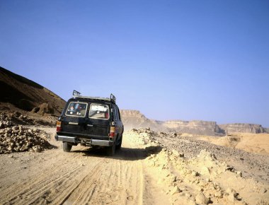 Çöldeki kayalık yığınlarda dört teker çekiş, arka planda parlak bulutlu gökyüzü, Yemen 'deki Arap çölünde tipik manzara.