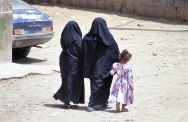 DARB AL HASHIMI,YEMEN-APRIL 15,2019: Veiled Muslim women walk on a street  with a little girl heading home 