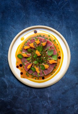 A plate of Marinated Tuna steak sliced, garnished with orange chutney, cilantro leaves, spring onion and a saltwort and chili flakes pesto. The recipe are seasoning with a vinaigrette of orange juice, olive oil, soy sauce and apple cider vinegar.