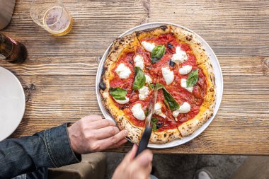 Erkek eller geleneksel Pizzeria 'nın ahşap bir masasında taze pişmiş Napoli Margherita pizzası kesiyor..