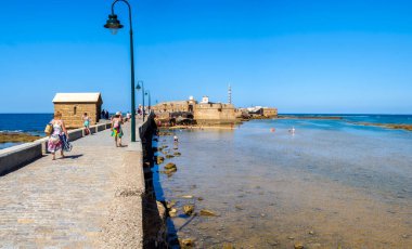 Cadiz, Spain - August 1, 2023. People enjoying a sunbathing in La Caleta beach, with the San Sebastian Castle, a fortress in La Caleta island, in the background. View from Paseo Fernando Quinones Promenade. Cadiz. Andalusia, Spain. clipart