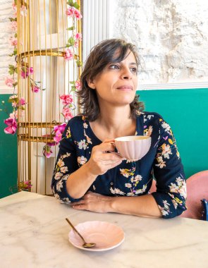 Beyaz, orta yaşlı bir kadın kahve dükkanında kahve içiyor..