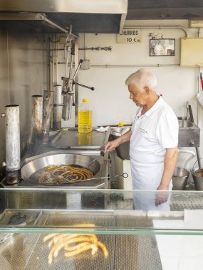 Cadiz, İspanya - 2 Ağustos 2023. Antonio, ünlü churrero (churro makinesi) ayçiçeği tohumları yağında churro tekerleği kızartıyor. Churreria Ana, Endülüs Cadiz 'deki Plaza de la Libertad Meydanı' nın bir büfesi..