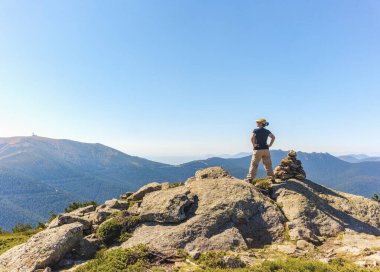 Orta yaşlı beyaz bir kadın bir dönüm noktasının yanındaki manzaraya hayran, bir dağın zirvesine çıktıktan sonra dinleniyor..