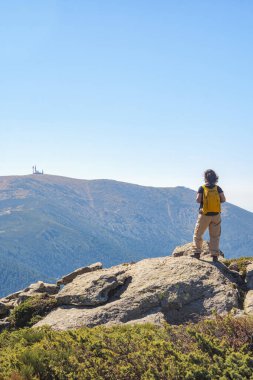 Orta yaşlı beyaz bir kadın bir dönüm noktasının yanındaki manzaraya hayran, bir dağın zirvesine çıktıktan sonra dinleniyor..