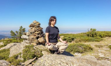 Orta yaşlı beyaz kadın, doğanın ortasında meditasyon egzersizi için bir kilometre taşının yanında oturuyor..