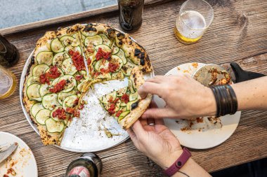 Erkek el, geleneksel Pizzeria 'da ahşap bir masada taze pişmiş bir Napoli kabağı pizzası alıyor..
