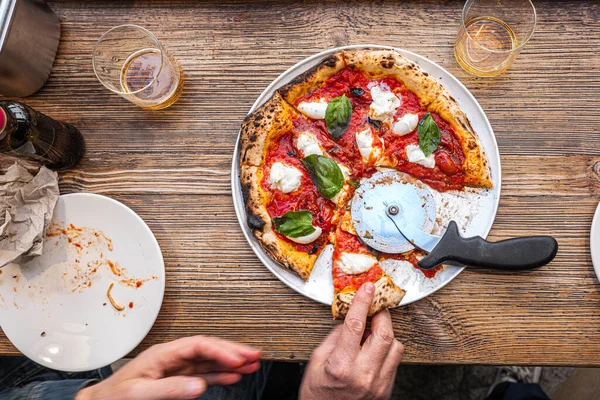 Erkek el, geleneksel Pizzeria 'daki ahşap bir masada taze pişmiş Napoli Margherita pizzasından bir dilim alıyor..