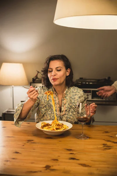 Gorgeous woman eating a plate of Tagliatelle al Ragu Bolognese in a cozy dining room; this traditional dish is part of Italian cuisine, and typically prepared with fresh pasta.