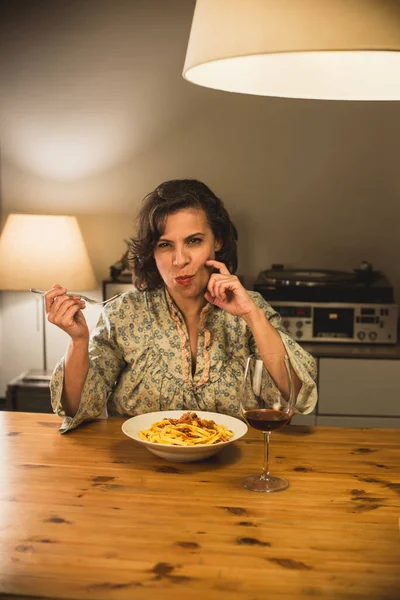Gorgeous woman eating a plate of Tagliatelle al Ragu Bolognese in a cozy dining room; this traditional dish is part of Italian cuisine, and typically prepared with fresh pasta.