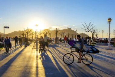 San Sebastian, Spain - March 13, 2024. People enjoying a sunset crossing La Concha Promenade at the level of the Don Quijote y Sancho Panza square. San Sebastian (Donostia), Basque Country, Gipuzkoa. Spain. clipart