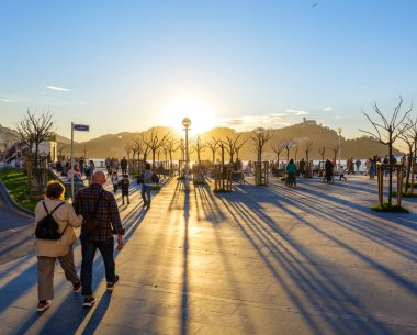 San Sebastian, Spain - March 13, 2024. People enjoying a sunset crossing La Concha Promenade at the level of the Don Quijote y Sancho Panza square. San Sebastian (Donostia), Basque Country, Gipuzkoa. Spain. clipart
