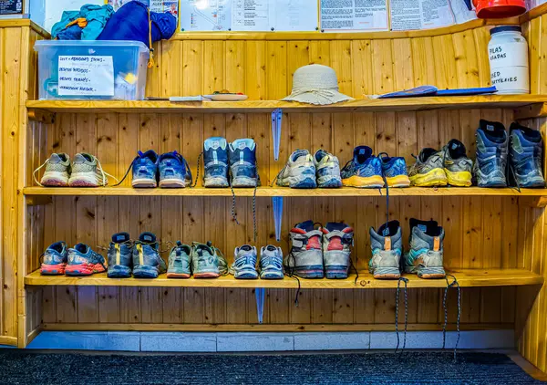 stock image Rabanal del Camino, Spain -  August 4, 2024.  A collection of worn and dirty hiking boots on wooden shelves at the entrance of a Camino de Santiago Albergue, showcasing the journey of pilgrims.