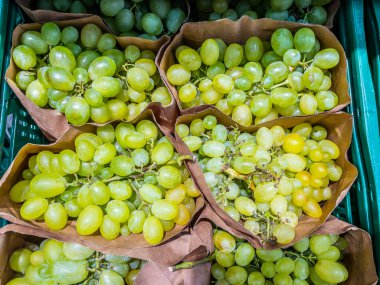 Bir markette kağıt torbalarda sergilenen taze yeşil üzümler. Üzümler olgun ve canlı. Tüketmek için mükemmel..