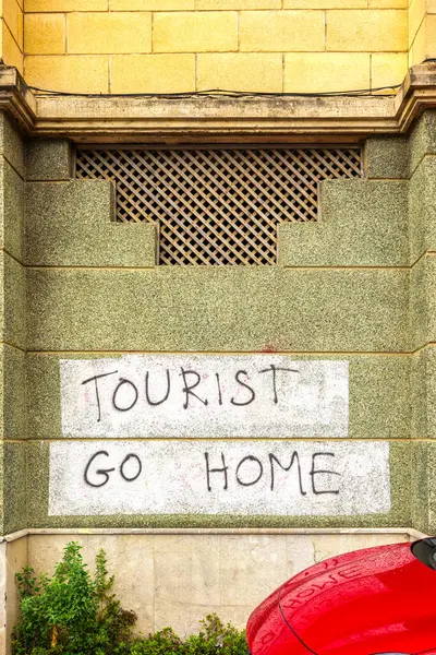 stock image Graffiti reading TOURIST GO HOME spray-painted on a stone building. The message reflects tensions between locals and tourists in popular destinations.