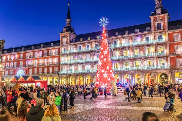 Madrid, İspanya - 18 Aralık 2023. Kutlama kalabalığı, arka planda Panaderia Casa de la Panaderia 'nın ana cephesi olan parlayan bir Noel ağacı tarafından aydınlatılan akşam saatlerinde Plaza Mayor' da toplanıyor. Madrid, İspanya.