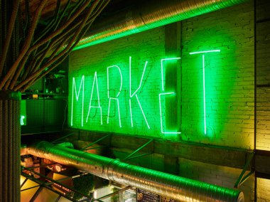 Madrid, İspanya - 11 Temmuz 2024. Yeşil neon MARKET işareti endüstriyel alanda tuğla duvarı aydınlatıyor. Açığa çıkan borular ve ipler görülebilir, atmosferik kentsel pazar ortamı yaratıyor.