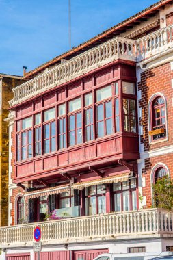 İspanyol balıkçılık bölgelerinde geleneksel bir binanın üst katından kırmızı boyalı ahşap bir balkon uzanır. Pencereleri, çizgili tenteleri, beyaz balkonu ve beyaz yüzeyli kırmızı tuğlası vardır..
