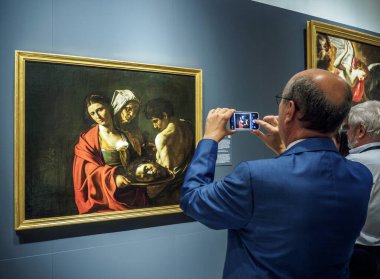 Madrid, İspanya - 24 Eylül 2024. Bir turist, Madrid Kraliyet Sarayı kompleksi Kraliyet Koleksiyonları Galerisi 'nde Caravaggio tarafından Vaftizci Yahya' nın Başkanıyla Salome 'nin fotoğrafını çekiyor..