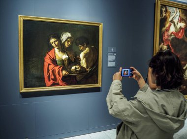 Madrid, İspanya - 24 Eylül 2024. Bir turist, Madrid Kraliyet Sarayı kompleksi Kraliyet Koleksiyonları Galerisi 'nde Caravaggio tarafından Vaftizci Yahya' nın Başkanıyla Salome 'nin fotoğrafını çekiyor..