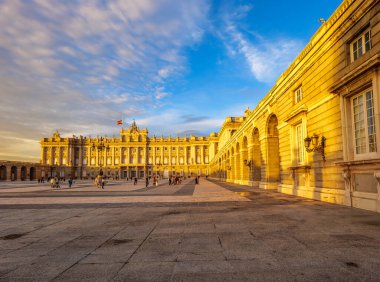 Madrid, Spain  November 1, 2024. Main facade of the Royal Palace under a warm sunset, with tourists exploring the Plaza de la Armeria. An iconic monument showcasing the architectural heritage of Spain. clipart