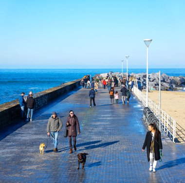 San Sebastian, İspanya - 19 Ocak 2025. İnsanlar Zurriola Breakwater boyunca köpeklerle yürüyüp deniz kenarında güneşli bir günün tadını çıkarıyorlar. San Sebastian, İspanya.