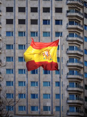 İspanya bayrağı açık bir günde yüksek bir şehir binasının önünde dalgalanıyor..