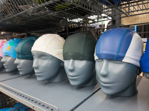 Swimming cap on mannequins for water sport display on shelves in sport shop.