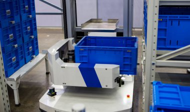 Modern endüstriyel depodaki çok katmanlı raflardan otonom robot malzemeleri topluyor..