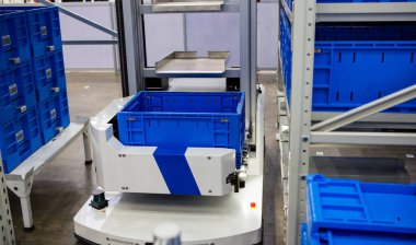 Modern endüstriyel depodaki çok katmanlı raflardan otonom robot malzemeleri topluyor..