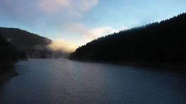 Sabahın erken saatlerinde sisli şafak ışıklarıyla bir gölün üzerinde uçmak. Hava aracı görünümü