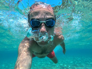 Yüzücü adam tropikal deniz suyunda sualtı selfie 'si çekiyor.