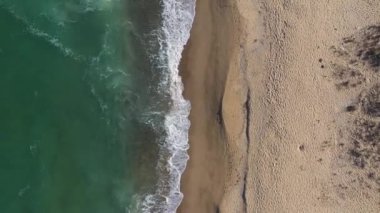 Deniz dalgalarının uzaktan kumlu bir sahile yaklaşan uzaktan görüntüsü.