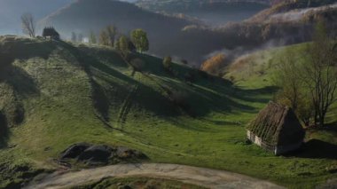 Dağ kulübesinin drone görüntüsü. Sonbaharda, sazdan çatısı olan terk edilmiş evlerle birlikte havanın sisli manzarası. Transilvanya, Romanya