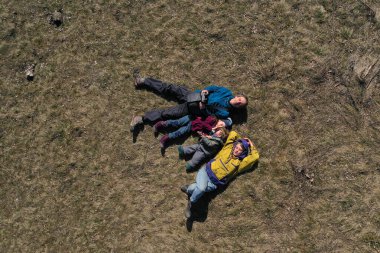 Anne, baba ve iki çocuğun çimenlerde yattığı mutlu bir ailenin insansız hava aracı görüntüsü.