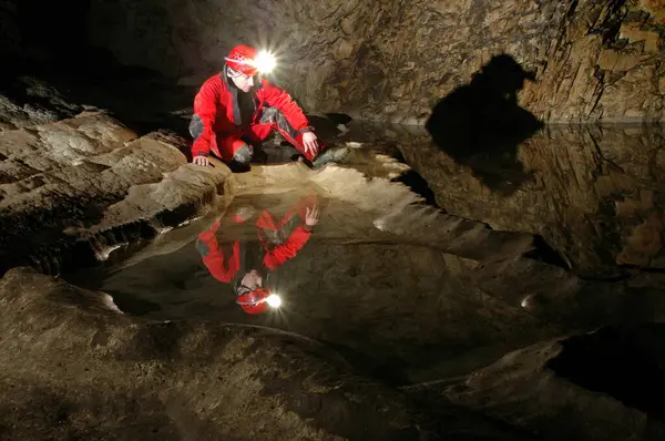 在洞穴的水池里反射出一个西班牙佬的影子 钢盔上的碳化物乙炔气体灯照亮了地下 免版税图库图片