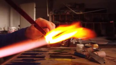 Bir atölyedeki gaz lambasının üzerinde duran cam boncuğu şekillendiren ellerin yakın plan çekimi. Cam işi mücevherler.