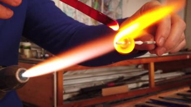 Sanatçı ellerinin yavaş çekim görüntüsü lamba çalışma tekniğiyle cam kolye yaratıyor. Gaz ocağı kullanarak cam ve alevi şekillendirmek.