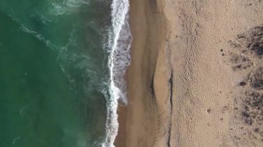 Uzaktan kumlu bir sahil ve insansız hava aracıyla deniz dalgalarının havadan yavaş çekim görüntüsü.