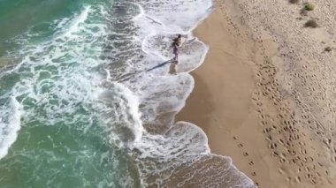 Kumsal manzarasında yürüyen sarışın manken kadın. Deniz dalgaları kumlu sahili İHA 'larla yıkıyor.
