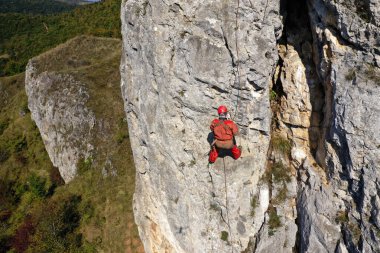 Aerial view of mountain rescuer abseiling on a rocky wall hanging on a rope clipart